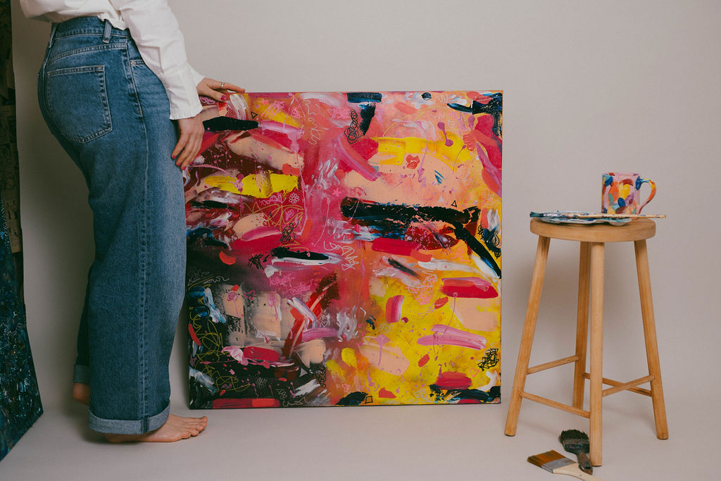 Kiri with an abstract painting in yellows, pinks and blacks